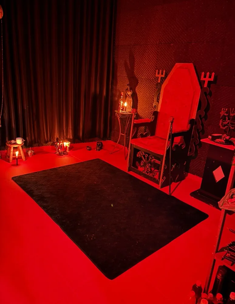 Trono de Exu Rei em madeira entalhada, ladeado por tridentes, com velas e oferendas acesas
